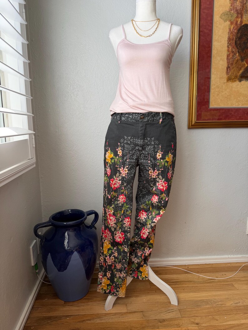 Puede incluir: Una camiseta de tirantes rosa p&aacute;lido combinada con pantalones gris oscuro con un estampado floral de rosas rojas, amarillas y rosas. Los pantalones tienen una cintura gris oscuro y un patr&oacute;n intrincado que se repite en la tela.