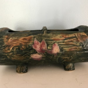 May include: A green and brown ceramic planter shaped like a log with pink flowers and three feet.