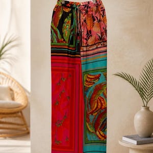 Puede incluir: Pantalones palazzo coloridos y estampados colgados de una percha negra. Los pantalones presentan una mezcla de colores y dise&ntilde;os vibrantes, incluyendo paneles rojos, rosas, turquesas y negros con estampados florales y abstractos. La palabra "arvin" es visible en la parte inferior.