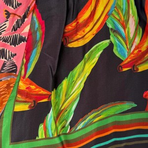 Puede incluir: Primer plano de una tela colorida con estampado tropical. El dise&ntilde;o presenta grandes hojas de pl&aacute;tano estilizadas en tonos amarillos, verdes y rojos sobre un fondo negro. La tela tambi&eacute;n tiene una secci&oacute;n rosa con un patr&oacute;n blanco y un borde a rayas.