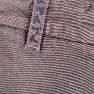 May include: Close-up of brown fabric with a textured weave. A belt loop is visible, featuring the embroidered word "AVA" in dark thread. The fabric appears to be a sturdy material, possibly denim or a similar textile.