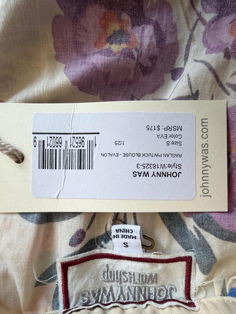 May include: A close-up of a floral print blouse with a tag. The tag reads "JOHNNY WAS" and "MADE IN CHINA". The blouse has a cream background with purple and orange floral patterns. The tag also shows the size as "S".