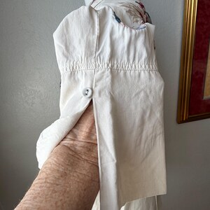 May include: Off-white button-down shirt with floral embroidery on the collar and shoulder. The shirt is displayed on a mannequin, with a buttoned cuff and a visible sleeve. The fabric appears to be cotton or a similar material.