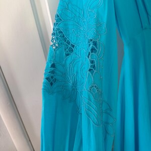 Puede incluir: Vestido turquesa de manga larga con intrincado bordado floral en la manga. El bordado presenta un dise&ntilde;o calado, a&ntilde;adiendo un toque delicado a la prenda. El vestido tiene una silueta fluida.