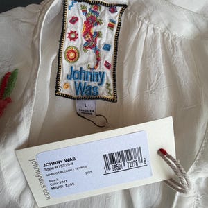 May include: White Margot blouse by Johnny Was, featuring an embroidered label with a colorful lizard design. The blouse has a tag with the brand name, style, size, and color information. The blouse is size L.