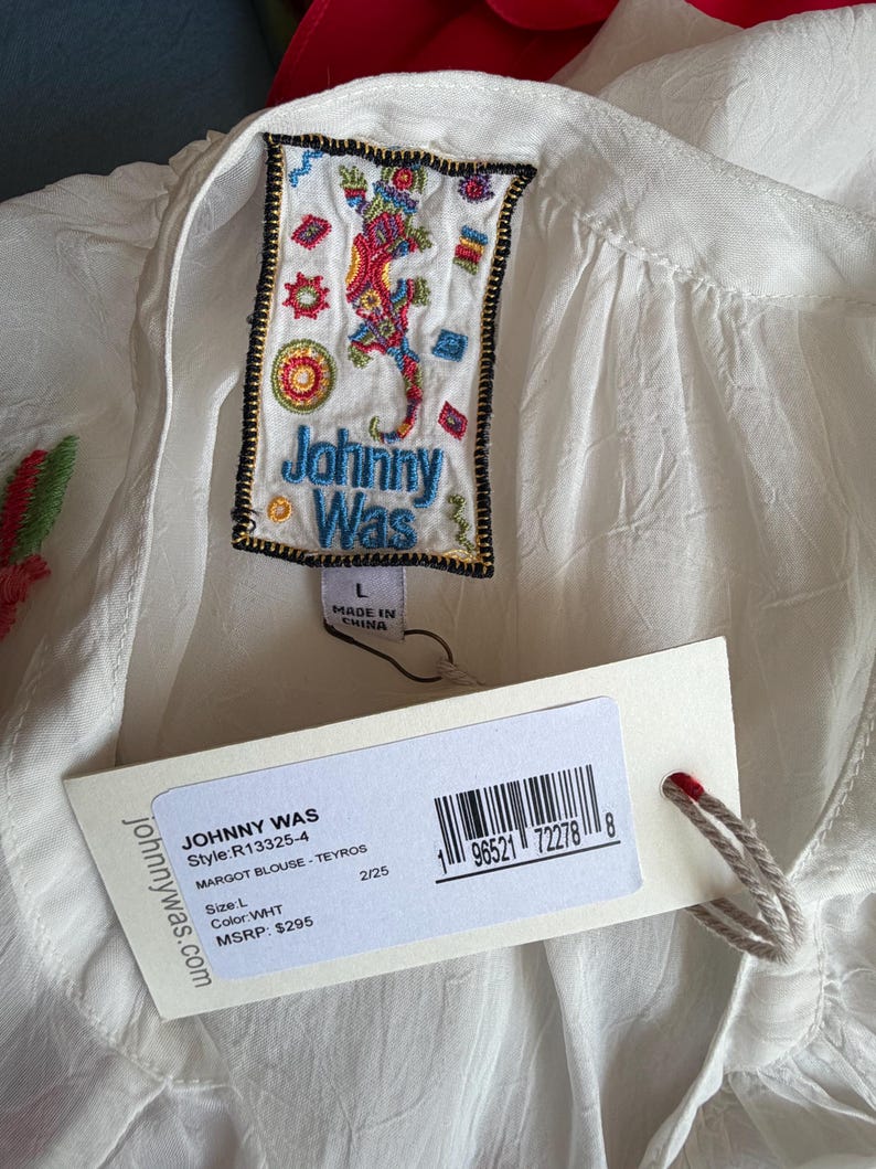 May include: White Margot blouse by Johnny Was, featuring an embroidered label with a colorful lizard design. The blouse has a tag with the brand name, style, size, and color information. The blouse is size L.