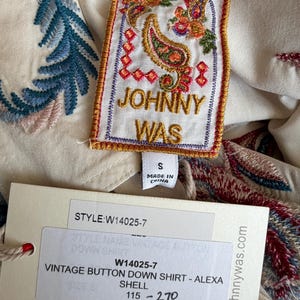 May include: Cream-colored vintage button-down shirt with colorful embroidered details. The shirt features a tag with the brand name "JOHNNY WAS" and the style information. The shirt is size small.