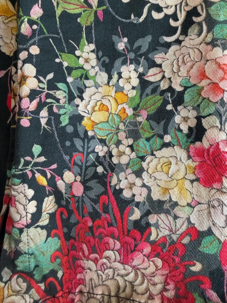 Puede incluir: Una tela negra con un estampado floral denso y multicolor. El patr&oacute;n incluye flores grandes y detalladas en tonos rojo, amarillo, crema y rosa suave, intercaladas con hojas verdes y tallos delicados sobre el fondo oscuro.