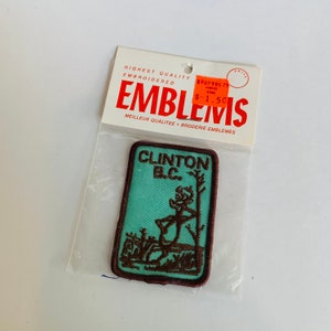 May include: A brown embroidered patch with a green background. The patch features a cartoon deer with the text "Clinton B.C." above it. The patch is packaged in a plastic bag with a price tag that reads "$1.50".