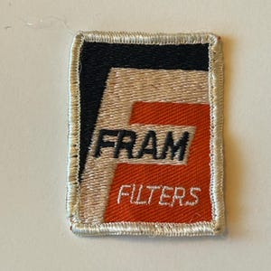 May include: A white and orange embroidered patch with the word "FRAM" in black lettering and the word "FILTERS" in white lettering.