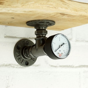 Può includere: Un supporto per mensola in metallo nero a forma di tubo con un manometro rotondo attaccato. Il manometro ha un quadrante bianco con segni neri e un ago nero. Il manometro legge in bar e ha una lettura massima di 4 bar.