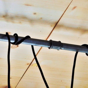 May include: Black metal pipe with flanges on each end, mounted to a wooden ceiling. Two black cords are wrapped around the pipe.
