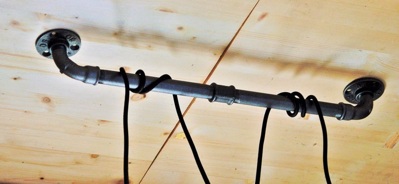 May include: Black metal pipe with flanges on each end, mounted to a wooden ceiling. Two black cords are wrapped around the pipe.