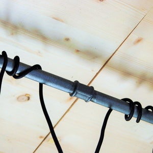 May include: A black metal pipe with two flanges on either end, mounted to a wooden ceiling. Two black cords are hanging from the pipe.