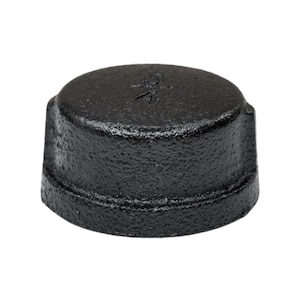 May include: A black, cast iron pipe cap with a textured surface. The cap is cylindrical with a flat top and a slightly raised rim. The cap is designed to seal the end of a pipe.