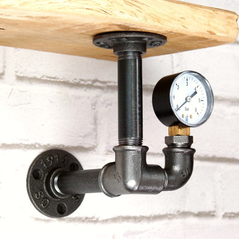 Puede incluir: Soporte de estante de tuber&iacute;a industrial negro con un man&oacute;metro. El man&oacute;metro tiene una esfera negra con n&uacute;meros blancos y una aguja blanca. El soporte del estante est&aacute; montado en una pared de ladrillo blanco.