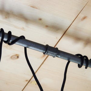 May include: Black pipe with black cords hanging from it, mounted to a wooden ceiling.