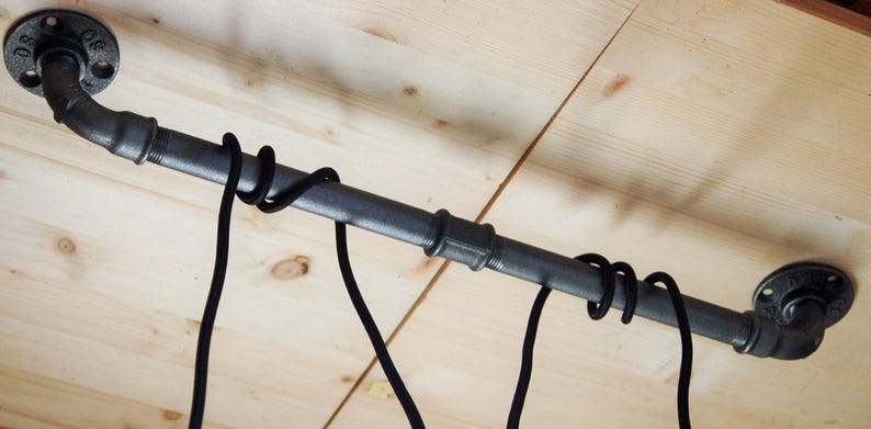 May include: Black pipe with black cords hanging from it, mounted to a wooden ceiling.