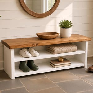 May include: A rectangular entryway bench featuring a natural wood top and a white base with two open shelves. The top shelf holds a wooden bowl and a potted succulent. The shelves contain white sneakers, a folded beige textile, and two books.