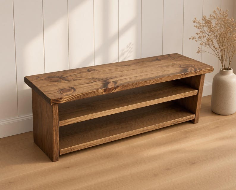 May include: A low rectangular wooden bench featuring a dark brown finish with visible wood grain and knots. The bench has a flat top surface and one open shelf underneath, supported by two solid side panels that extend to the floor.