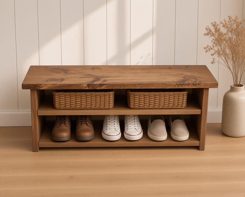 May include: A rectangular wooden shoe bench with a dark brown stained finish, featuring a flat top surface, one middle shelf holding two woven wicker baskets, and a bottom shelf containing three pairs of shoes in brown, white, and beige.