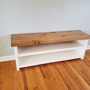 May include: A white wooden bench with a natural wood top and two shelves. The bench is sitting on a hardwood floor.