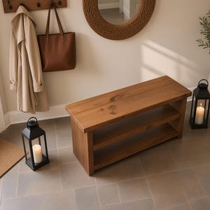 May include: A rectangular wooden bench featuring a natural brown finish with visible wood grain and a single lower shelf for storage. The bench is constructed from solid planks and has a smooth, flat top surface with a sturdy, block-style base design.