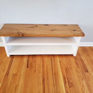 May include: A white wooden bench with a natural wood top. The bench has two shelves for storage.