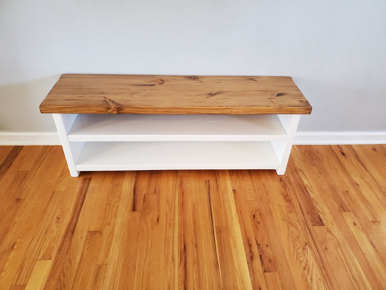 May include: A white wooden bench with a natural wood top. The bench has two shelves for storage.