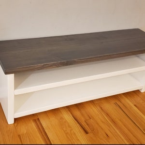 May include: A white wooden bench with a gray stained top and two shelves. The bench is made of wood and has a simple design.