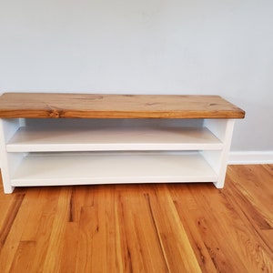 May include: A white wooden bench with a natural wood top and two shelves. The bench is sitting on a hardwood floor.