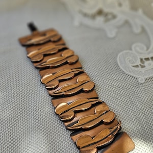 May include: A vintage copper bracelet featuring rectangular links with leaf-like patterns. The bracelet has a reddish-brown colour and a clasp. The design is Art Deco inspired. The bracelet's length is approximately 18 cm.