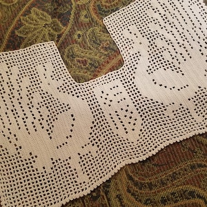 May include: A white crocheted doily with a scalloped edge. The doily features a design of two stylized birds.