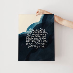 May include: A rectangular art print featuring a dark navy blue watercolor wash background with white cursive text that reads: When peace like a river, attendeth my way, when sorrows like sea billows roll; whatever my lot, Thou hast taught me to say, it is well, it is well, with my soul.