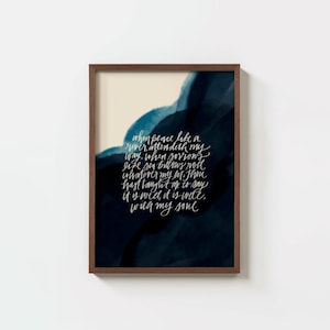 May include: A framed wall art print featuring white cursive calligraphy text on a dark navy blue and cream watercolor background. The text reads: When peace like a river, attendeth my way, when sorrows like sea billows roll; whatever my lot, Thou hast taught me to say, it is well, it is well, with my soul.