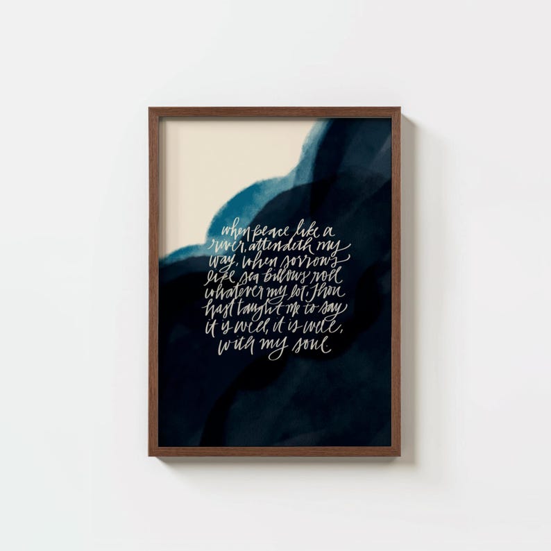 May include: A framed wall art print featuring white cursive calligraphy text on a dark navy blue and cream watercolor background. The text reads: When peace like a river, attendeth my way, when sorrows like sea billows roll; whatever my lot, Thou hast taught me to say, it is well, it is well, with my soul.