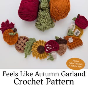 May include: A crochet garland pattern featuring autumn-themed motifs including a pumpkin, pie, sunflower, mushroom, acorn, and apple. Three skeins of yarn in red, green, and orange are positioned above the crocheted items. Text reads: Feels Like Autumn Garland Crochet Pattern. Photos, Video Tutorials, & Helpful Tips!