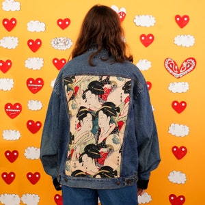 May include: A denim jacket with a colorful Japanese-inspired print on the back. The print features women in traditional clothing and flowers.