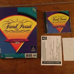 May include: A box and CD-ROM case for the computer game Trivial Pursuit CD-ROM Edition. The box is yellow, red, and blue with the game's logo and title. The CD-ROM case is black with a blue, yellow, and red design and the game's title.