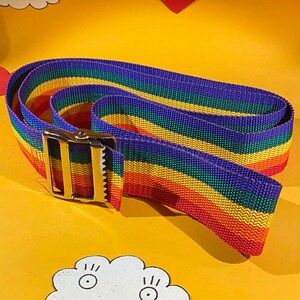 May include: A rainbow-colored nylon strap with a silver buckle. The strap is folded in half and the buckle is on the outside of the strap.