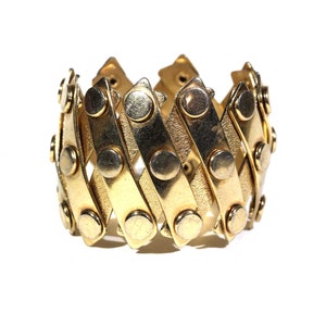 May include: A gold-toned bracelet with a flexible design. The bracelet is made of interlocking metal strips with round, raised accents.