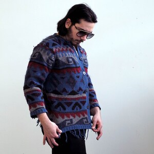 May include: A blue, red, and black patterned cardigan with a button closure. The cardigan has a fringed hem and is made of a soft, knitted fabric.