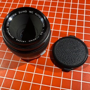 May include: A black Olympus OM-System Zuiko MC Auto-Macro 1:3.5 f=50mm 1:81006 lens with a black lens cap.