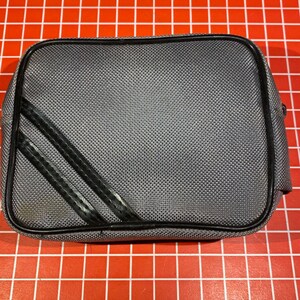 May include: A gray zippered pouch with black trim and two black stripes. The pouch is made of a textured fabric.