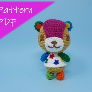 May include: Crochet pattern PDF for a colourful animal character with a pink head, brown body, and white face. The character is wearing a white shirt with colourful stars and has green and orange legs.