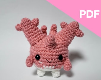 May include: A pink crocheted amigurumi toy with white feet and black eyes. The toy has a unique, spiky design and a friendly expression.