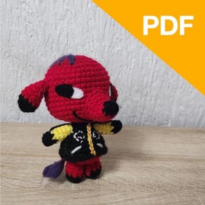 Könnte beinhalten: Gehäkelte Figur eines roten, hundeähnlichen Charakters mit schwarzen und weißen Akzenten. Die Figur trägt eine schwarze Jacke mit gelben Ärmeln und einen lila Schwanz. Das Wort "PDF" ist oben rechts zu sehen.