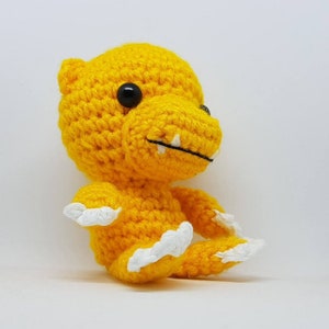 K&ouml;nnte beinhalten: Ein gelbes H&auml;kel-Dinosaurierspielzeug mit wei&szlig;en Krallen und schwarzen Augen.