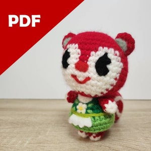 May include: Crocheted amigurumi toy of a red squirrel wearing a green dress with a white flower. The toy has black eyes and a white face.