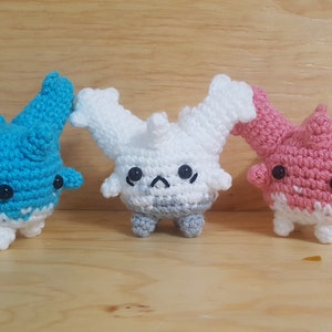 May include: Three crocheted plushies in the shape of a creature with a round body and multiple arms. The plushies are blue, white, and pink.